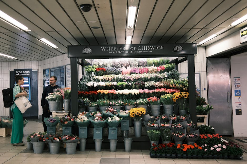 A vibrant display of fresh flowers at Wheeler of Chiswick’s flower stall in a London underground station with a variety of blooms including roses, tulips, daffodils, and hyacinths in shades of pink,