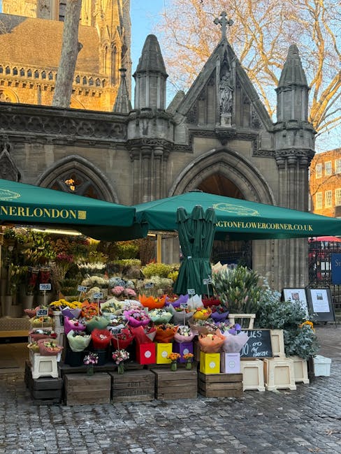 A vibrant outdoor flower stall situated in front of a historic stone building with Gothic architectural features, including arched windows and turrets, at London Fields station. The display showcases