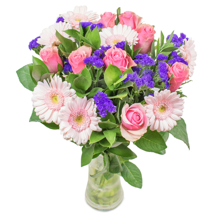 A vibrant, expertly crafted bouquet arranged in a crystal-clear glass vase, set before a clean, white backdrop that highlights every shade and contour of the blooms. This Hackney arrangement features a blend of seven to nine classic pink roses, their petals spiraled tight or just beginning to unfurl-capturing the moment before full bloom in a gesture both hopeful and refined. Interlaced among these, five to seven pale pink gerbera daisies display their large, round faces and whisper-soft petals, their centers a breath lighter, lending dimension and visual sweetness. Bright, dramatic clusters of purple statice weave through the bouquet, offering a contrast reminiscent of Hackney's vibrant creative scene and adding both texture and a deeper hue to the display. Anchoring the design, rich green foliage creates a base that feels abundant and fresh, its glossy leaves peeking just beyond the petals and recalling the tidy community gardens of the borough. The transparent vase reveals water and meticulously trimmed stems, suggesting arrival as a fresh flower delivery-perhaps for a birthday gathering near Mare Street or an anniversary celebration in London Fields. This composition balances grace and exuberance, expressing joy, affection, and the warmth of Hackney's local spirit.